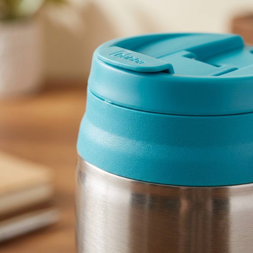 Close-up of the teal flip-top lid and brushed stainless steel rim on a bubba Classic Insulated Mug.
